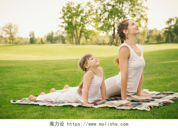 日落时年轻的母亲和女儿在城市公园做瑜伽运动双人瑜伽